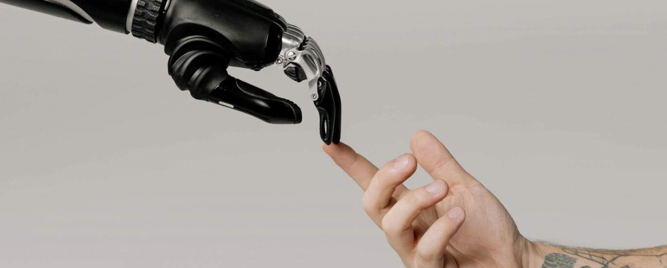 A human hand with tattoos reaching out to a robotic hand on a white background.