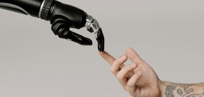 A human hand with tattoos reaching out to a robotic hand on a white background.