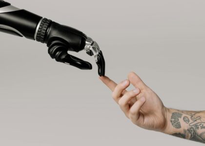 A human hand with tattoos reaching out to a robotic hand on a white background.