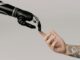 A human hand with tattoos reaching out to a robotic hand on a white background.