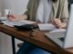A woman manages finances at home, using a laptop and calculator on a wooden desk.