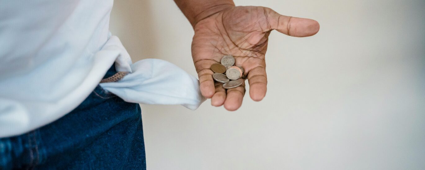 A close-up of a person holding coins with a turned-out empty pocket, illustrating financial struggle.